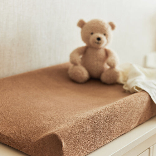 Jollein badstof verschoonkussenhoes in biscuitkleur op een commode met een teddybeer.