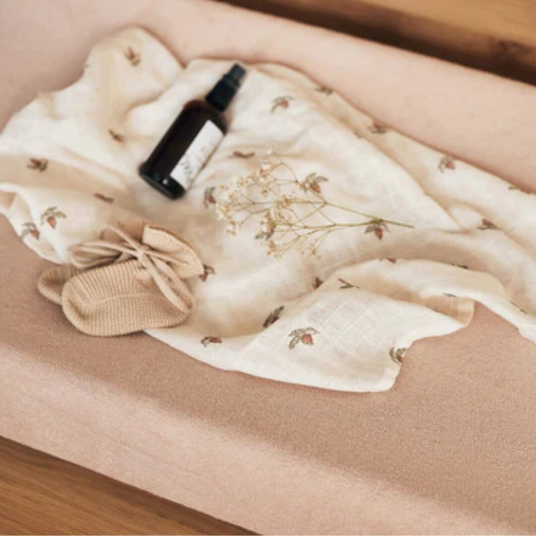 Jollein badstof hoes voor verschoonkussen in wild rose met een hydrofiele doek, flesje en babyschoentje erop.