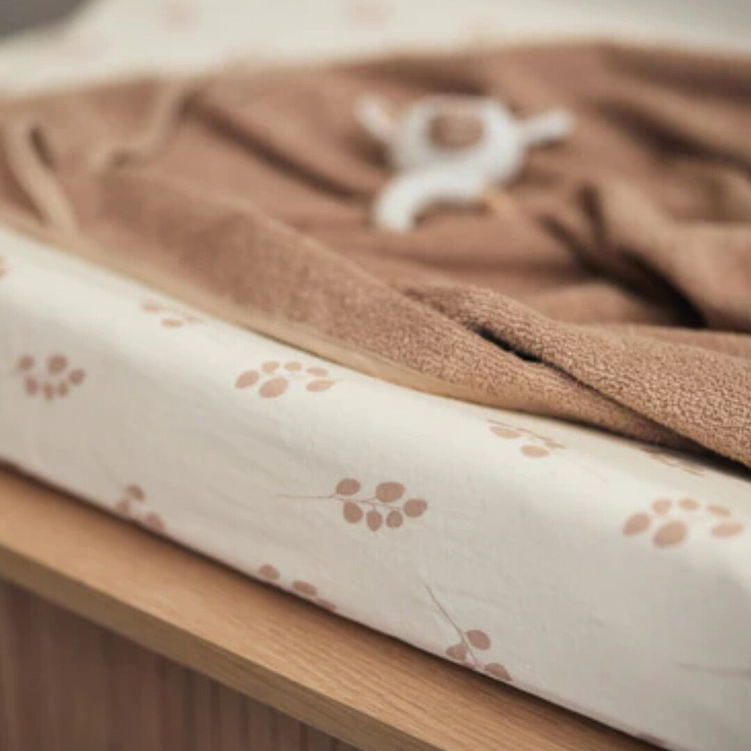 Jollein hoes voor een verschoonkussen met wild rose takjespatroon op een commode met handdoek en babyspeeltje.