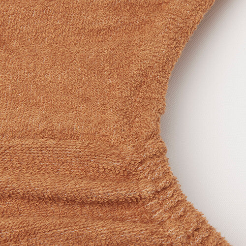 Close-up van de elastische rand en badstof textuur van een caramelkleurige verschoonkussenhoes.