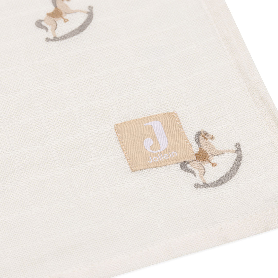 Close-up van een Jollein hydrofiele multidoek met schommelpaardjespatroon en merklabel.