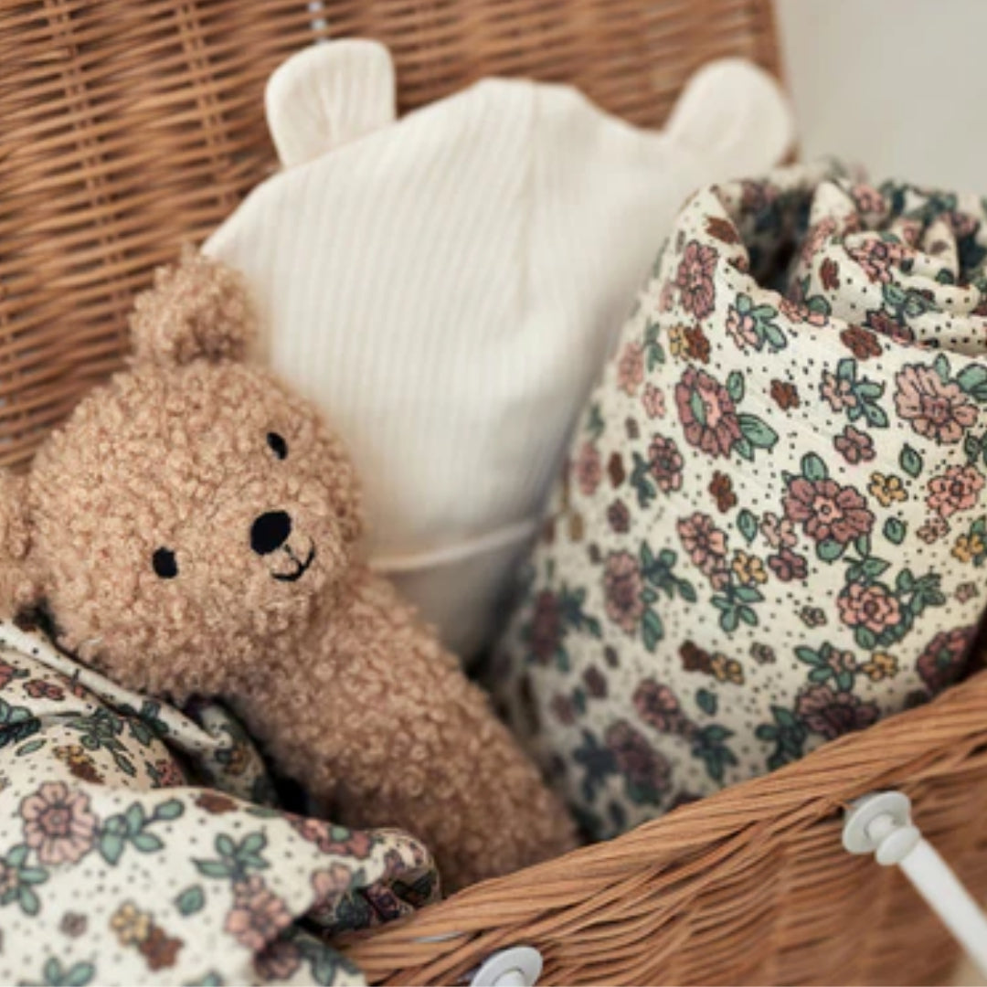 Een Jollein hydrofiele multidoek met retro bloemenpatroon, een teddybeer en een muts in een rieten mand.