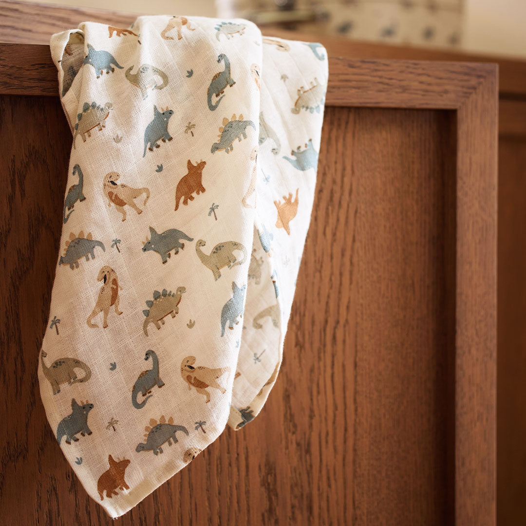 Een Jollein hydrofiele multidoek met dinosauruspatroon hangt over een houten rand.
