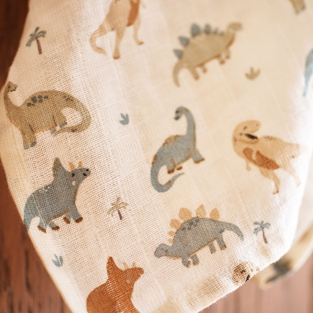 Close-up van een Jollein hydrofiele multidoek met beige, blauwe en bruine dinosaurussen en palmboompjes.