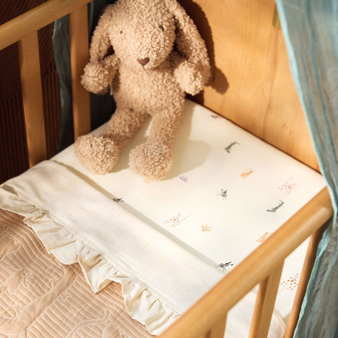 Jollein kinderhoeslaken met jungle dierenpatroon op een ledikantmatras, met een knuffelkonijn.