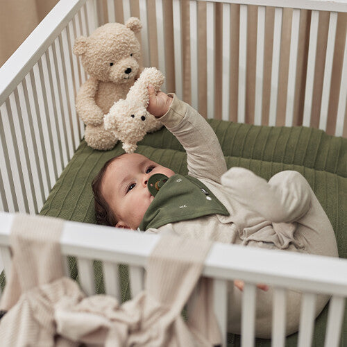 Een baby in een wieg speelt met de jollein knijprammelaar teddybeer.