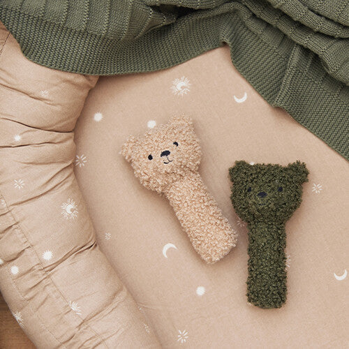 Twee Jollein knijprammelaars teddybeer, één beige en één groen, liggen op een babybedje.
