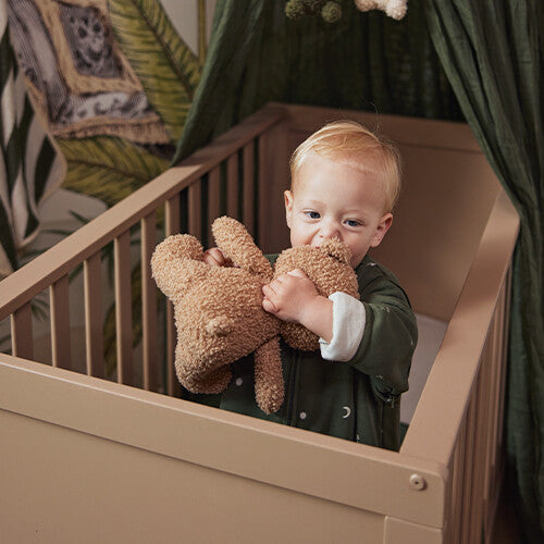 Een baby in een ledikantje speelt met de Jollein pluchen knuffelbeer.