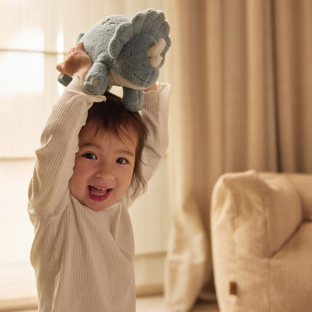 Een lachend kind houdt de Jollein pluchen triceratops knuffeldino boven haar hoofd.