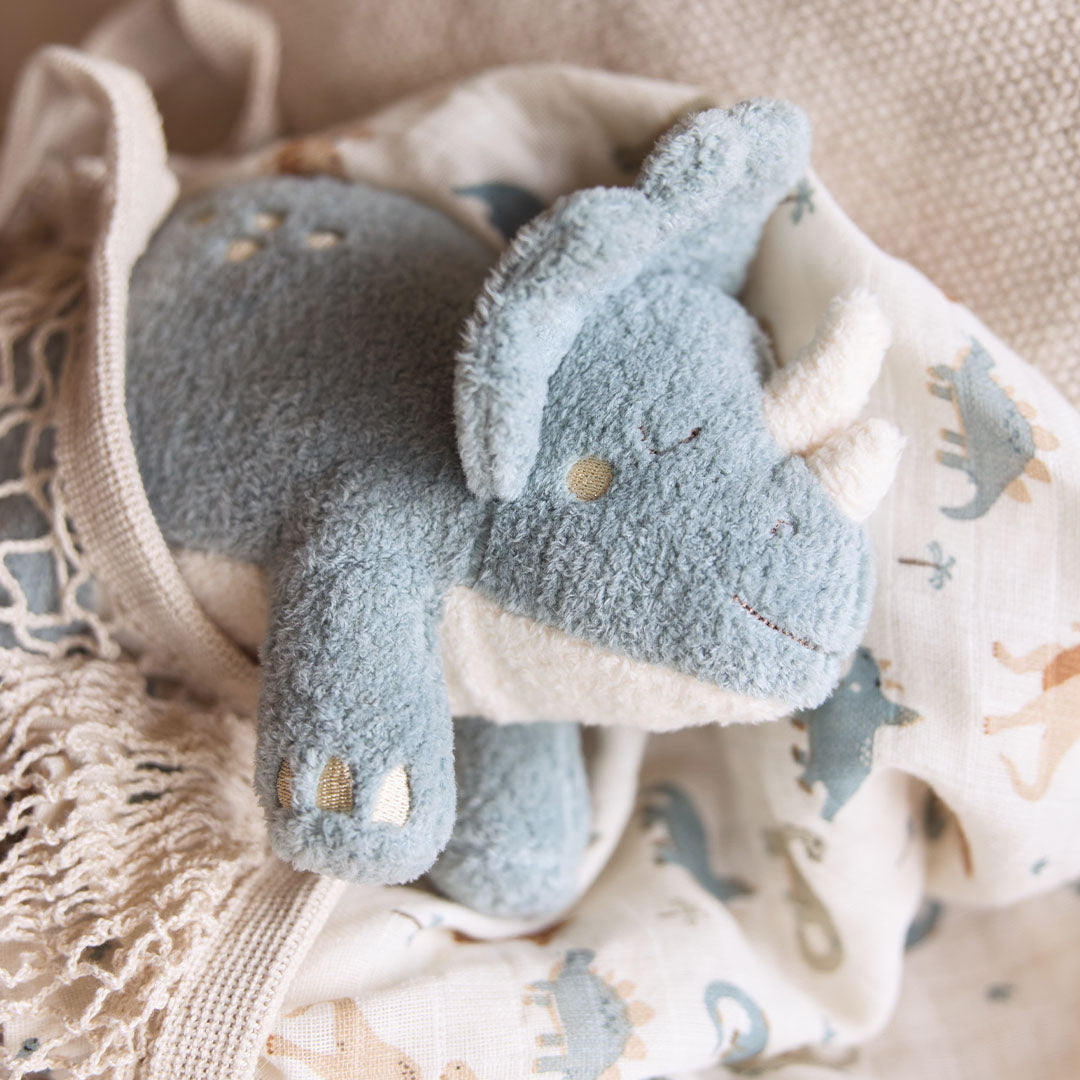De Jollein pluchen triceratops knuffeldino ligt op een deken met dinoprint, deels onder een netje.