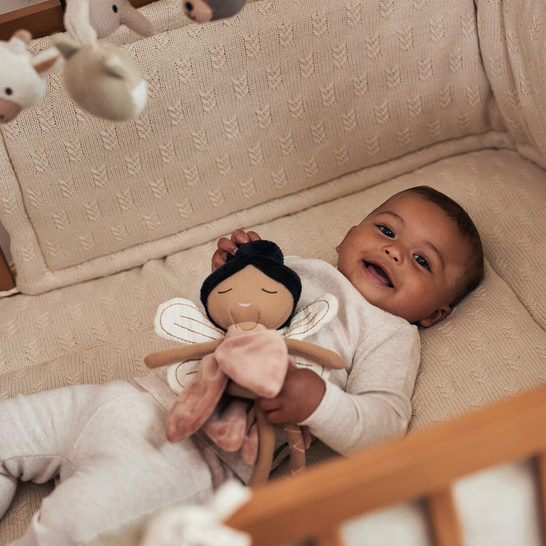 Een lachende baby ligt in een wieg en knuffelt de Jollein lappenpop elfje Mae.