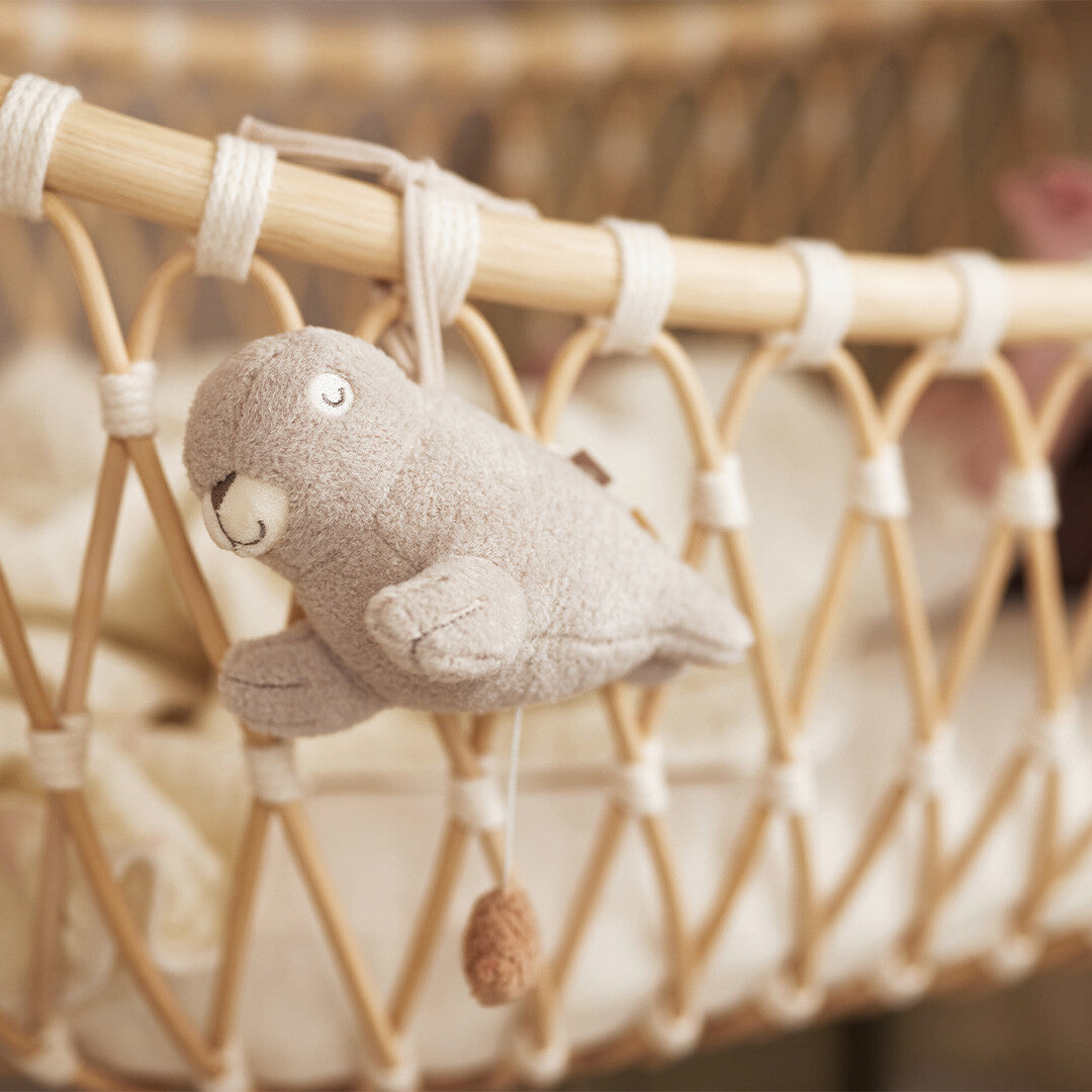 Jollein pluchen zeehond muziekdoosje hangend aan een rotan babywiegje.