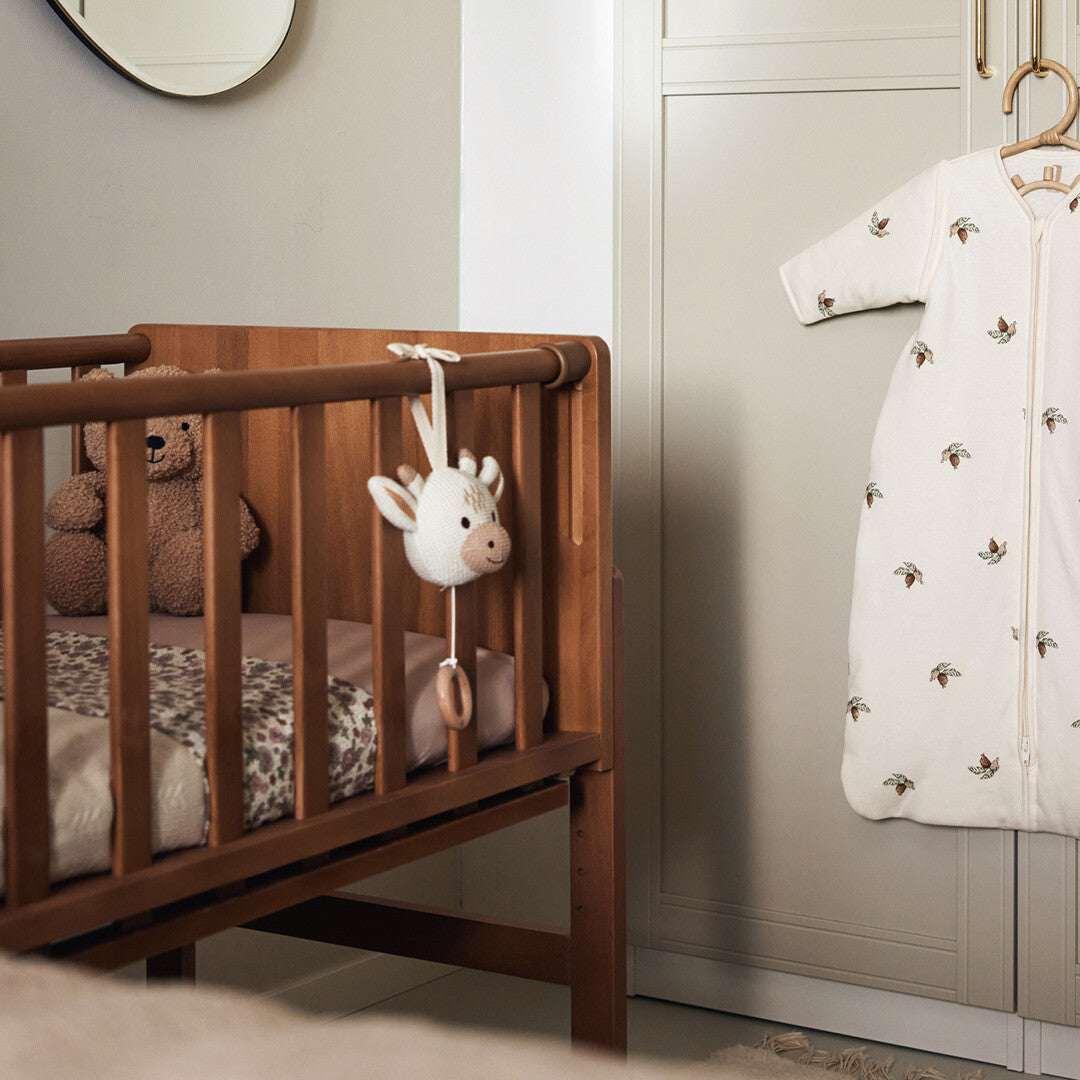 Jollein babyspeelgoed muziekdoosje in de vorm van een gebreide giraffenkop hangt aan de zijkant van een houten babybedje.