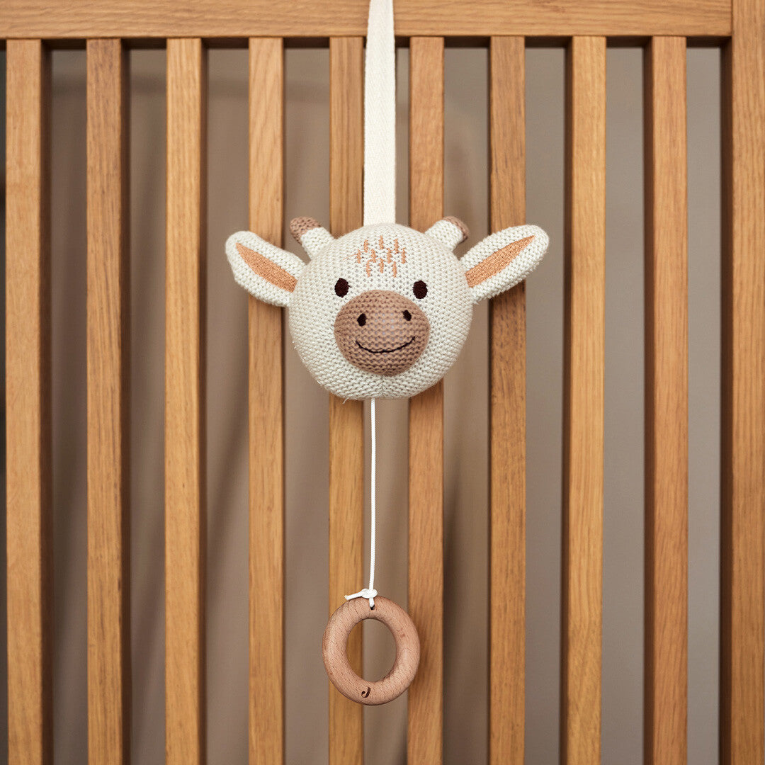 Jollein babyspeelgoed muziekdoosje in de vorm van een gebreide giraffenkop met houten ring, hangend aan de houten spijlen van een babybedje.