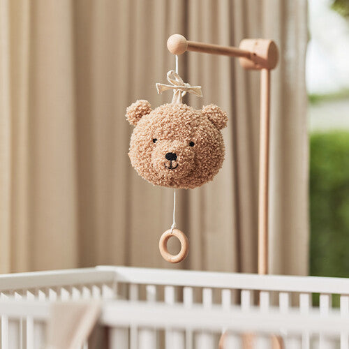 Het Jollein muziekdoosje teddybeer hangt aan een houten mobile boven een wit babybedje.