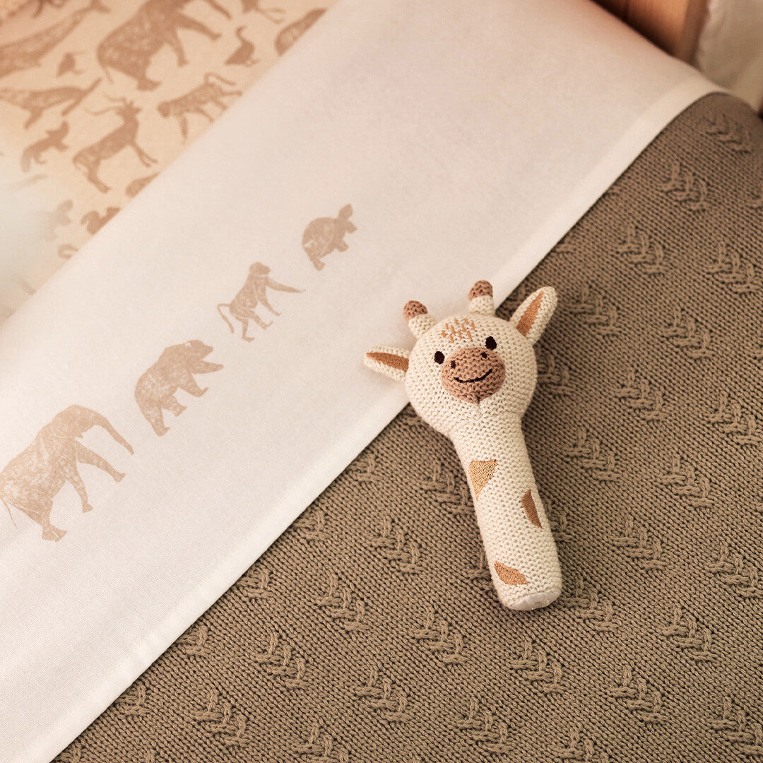 Jollein giraffe rammelaar op een bruine gebreide deken naast een wit laken met safari dieren.