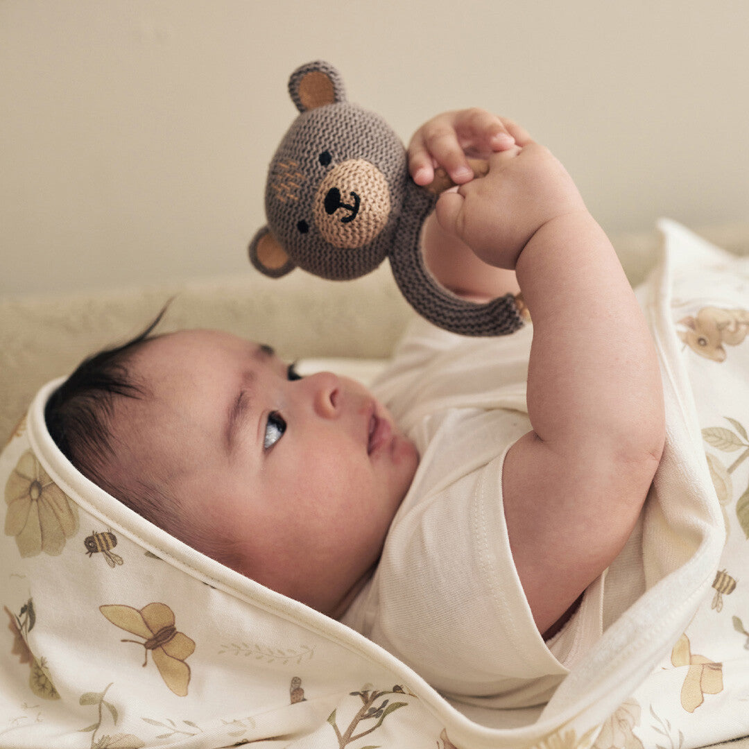 Een baby ligt op de rug en houdt de Jollein rammelaar met bijtring beer boven zich.