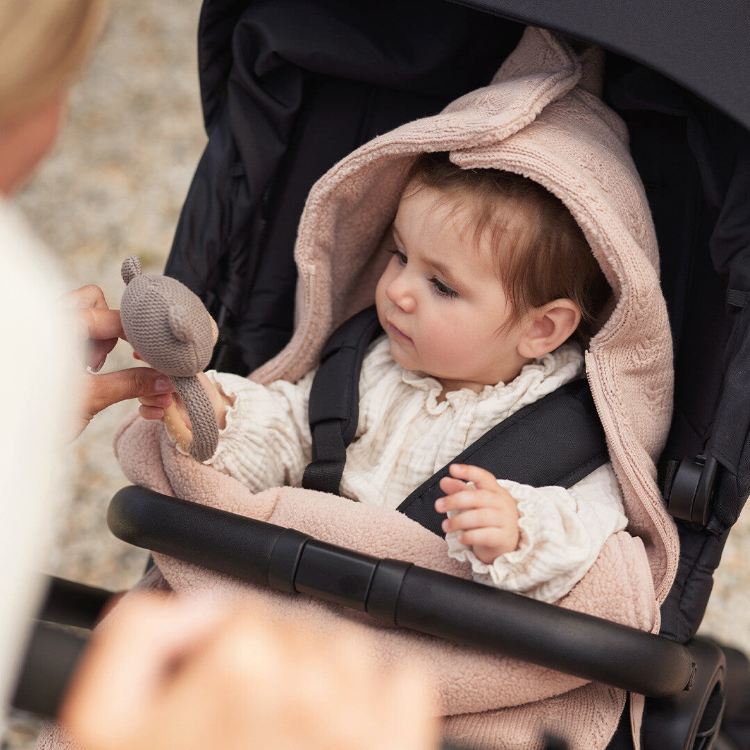 Een baby in een kinderwagen kijkt naar de rammelaar met bijtring beer die een volwassene vasthoudt.