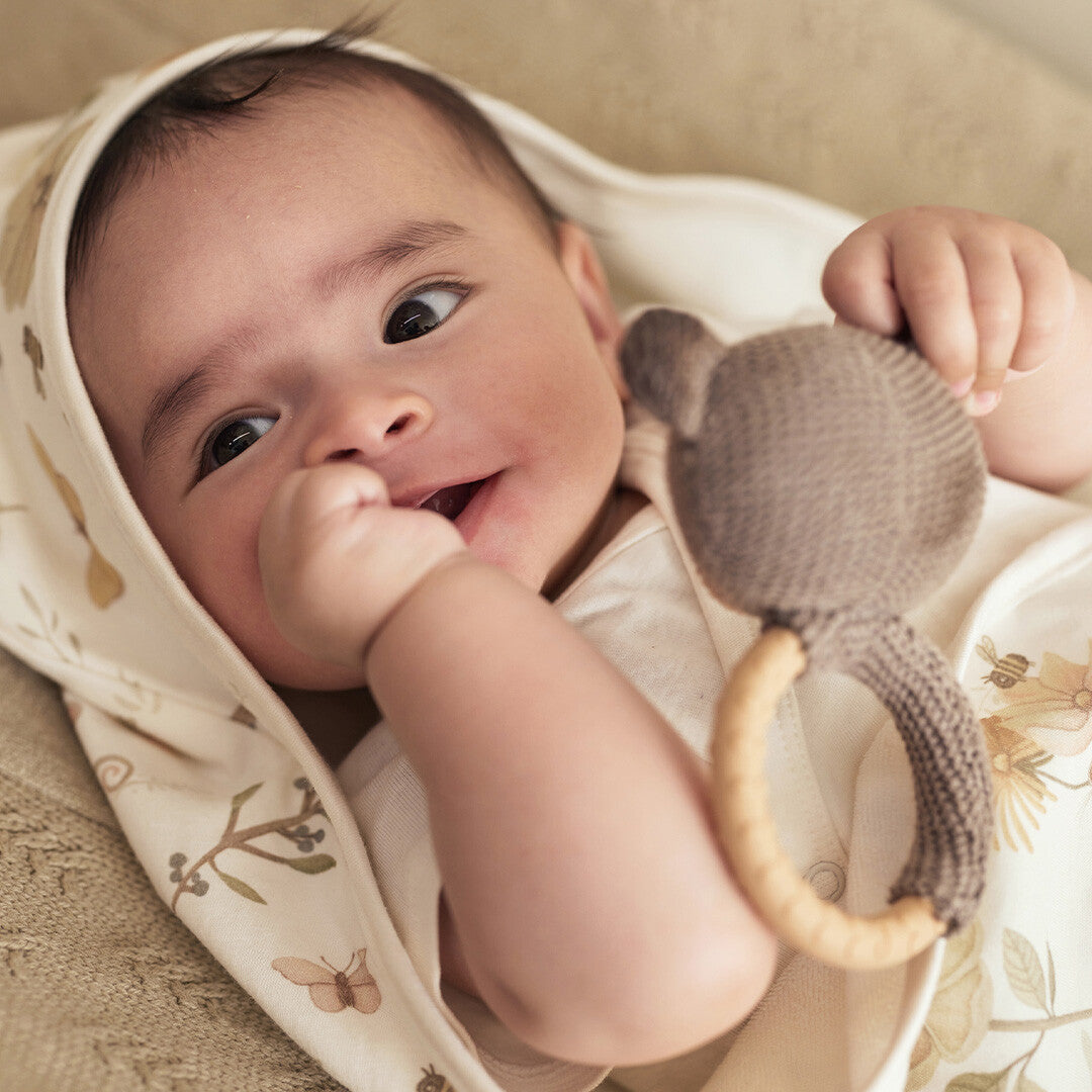 Een baby ligt op de rug en houdt de rammelaar met bijtring beer bij de mond.