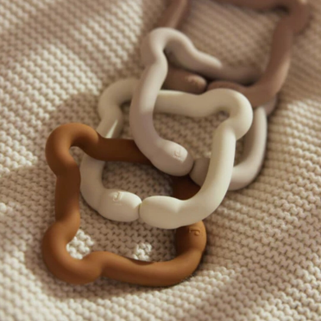 Jollein siliconen bijtspeelgoedringen in teddy bear vorm, in verschillende kleuren, liggend op een gebreide deken.