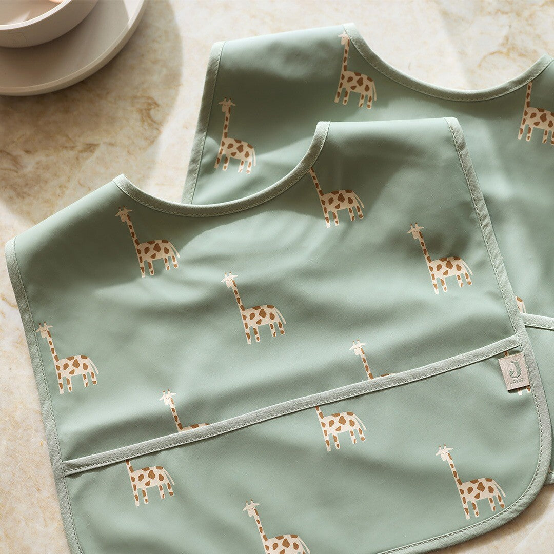 Detail van twee Jollein waterdichte babyslabbetjes met groen giraffenpatroon.