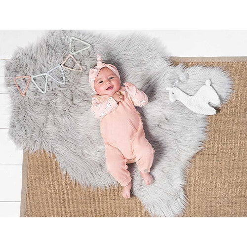Een lachende baby ligt op een kleed naast de Jollein off-white pluchen lama speendoek.