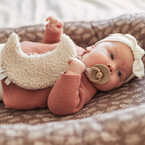 Een baby ligt op haar rug en houdt de Jollein maan speendoek vast.