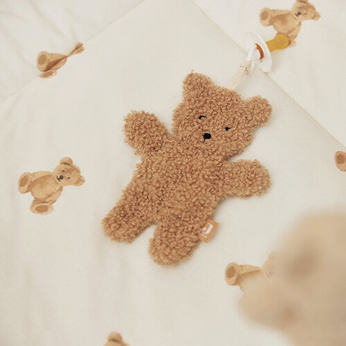 Het Jollein teddy bear speendoekje ligt op een deken met berenpatroon, bevestigd aan een speen.