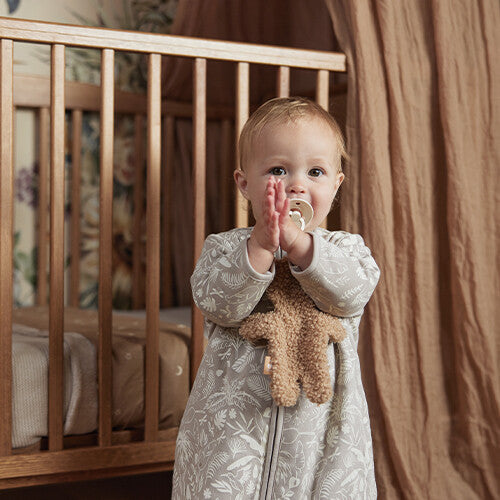 Een baby staat in een ledikantje met het Jollein teddy bear speendoekje tegen de borst.