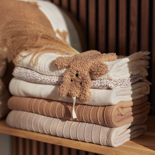 Het Jollein teddy bear speendoekje ligt bovenop een stapel opgevouwen babydekens.