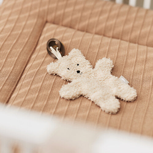 De jollein teddybeer speendoek met speen ligt op een geribbeld bruin matras in een wieg.