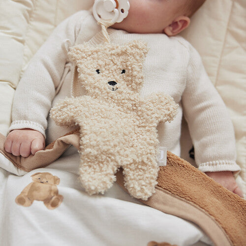 Close-up van een baby met de jollein teddybeer speendoek aan een speen op de borst.