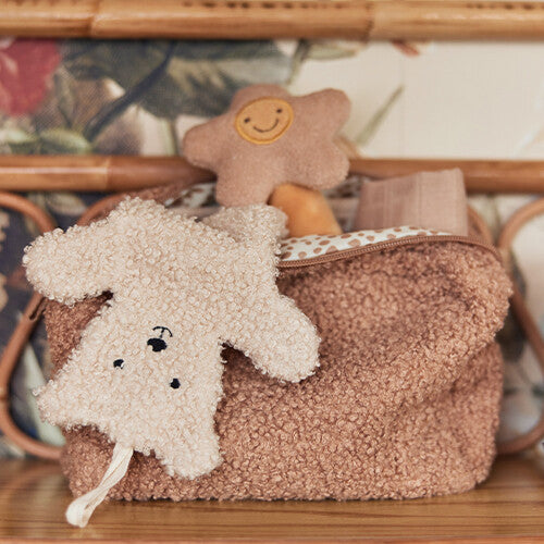 De jollein teddybeer speendoek hangt aan een bruine toilettas, naast een ster-vormige rammelaar.