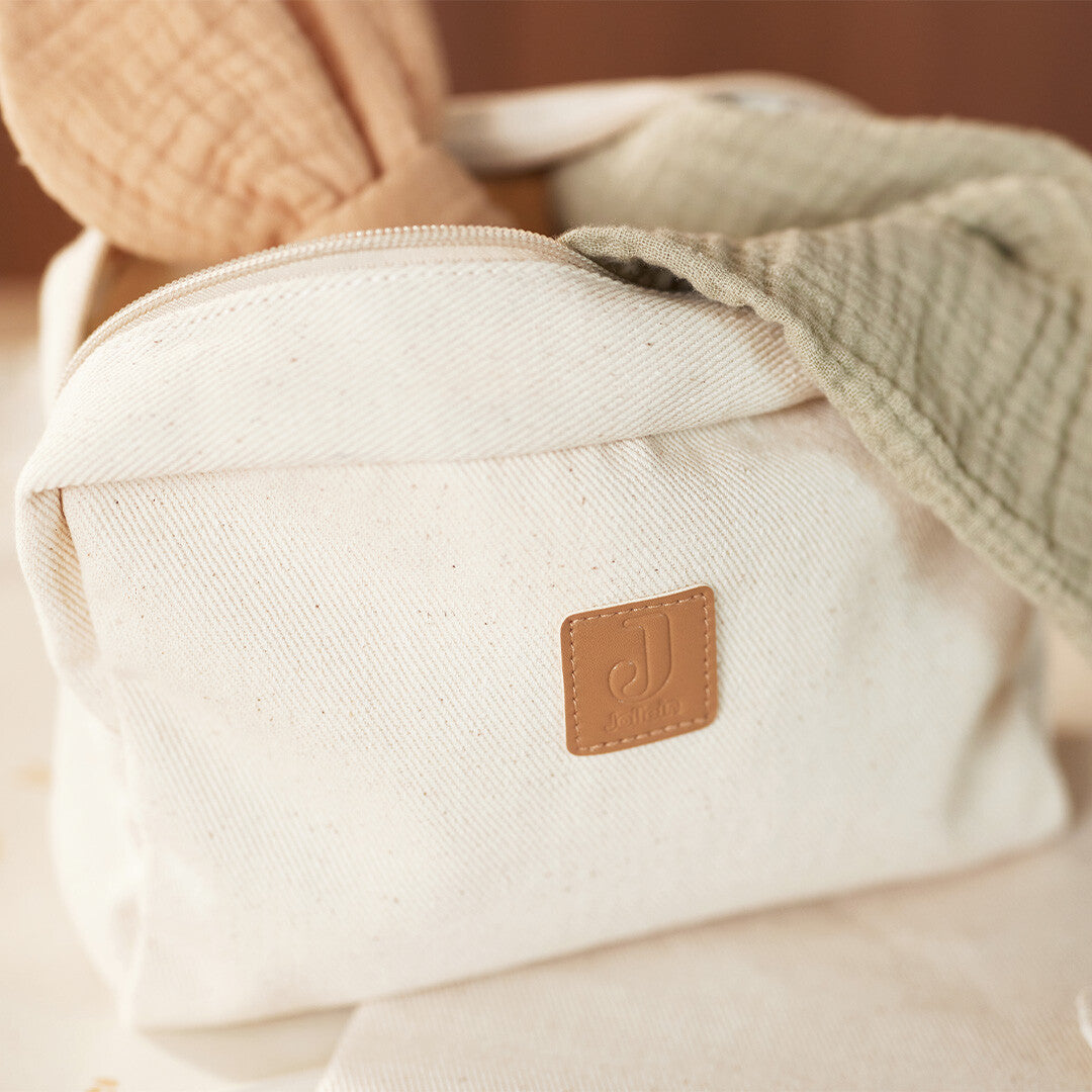Jollein beige twill toilettas met logo, gevuld met een konijnenrammelaar en een groene hydrofiele doek.