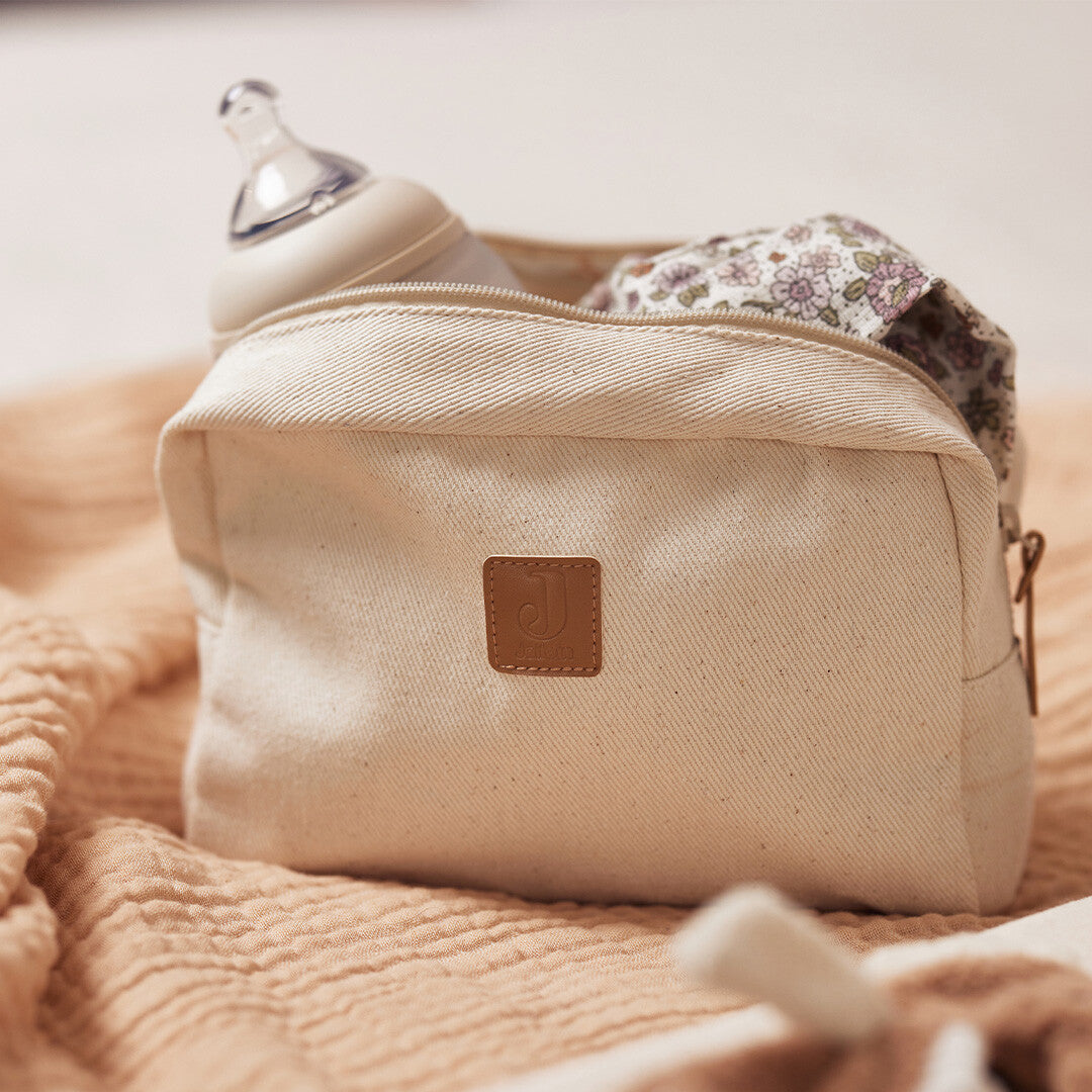 Jollein beige twill toilettas op een deken, gevuld met een babyfles en een doek met bloemenprint.
