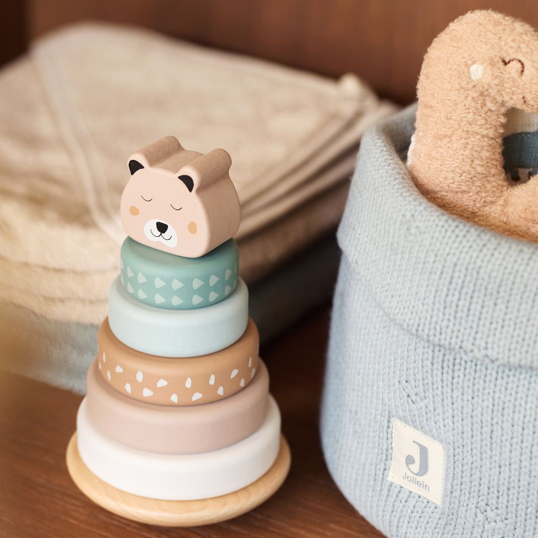 Jollein houten tuimelstapelaar met beerkop staat naast een blauwe opbergmand met knuffel.