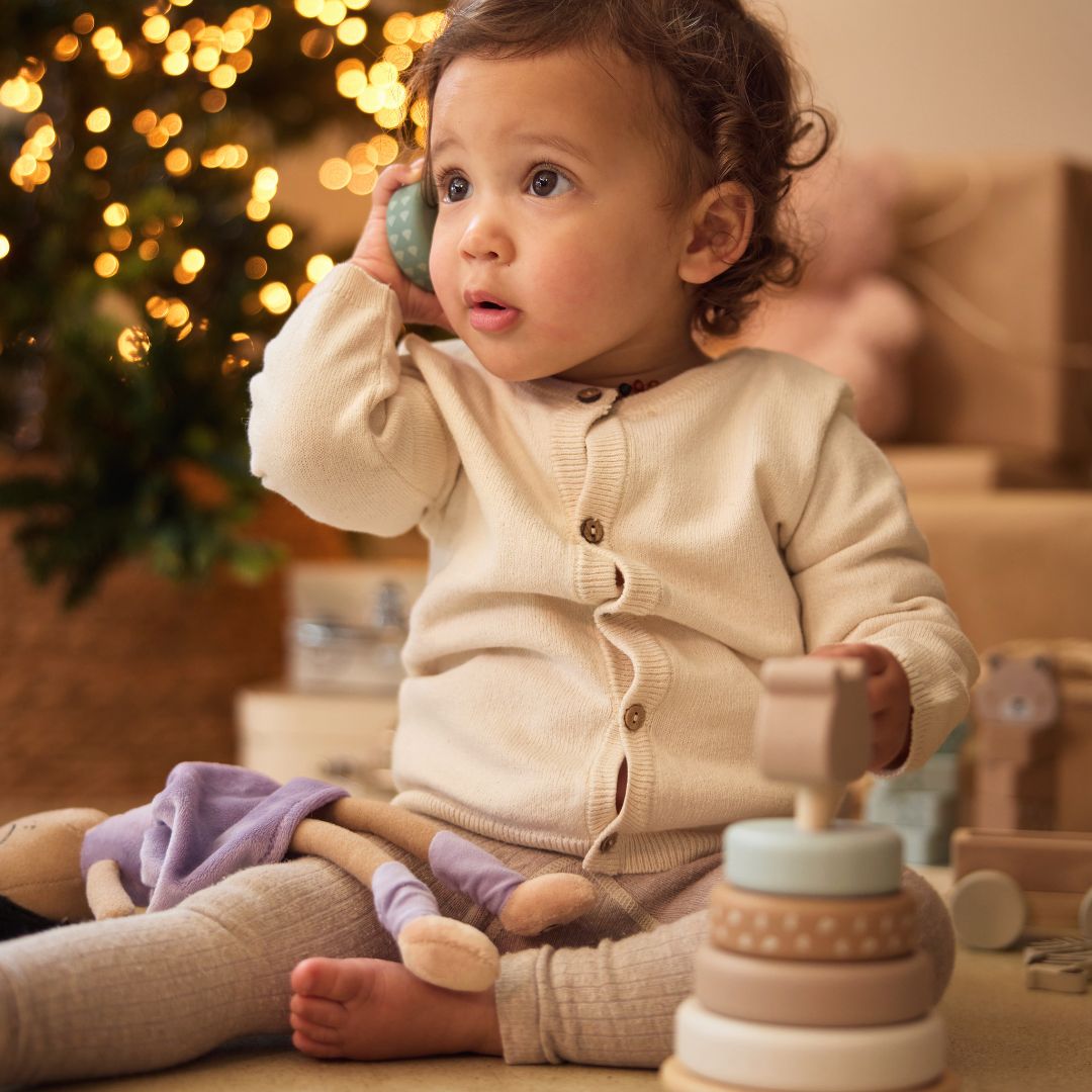 Een baby speelt met een ring van de Jollein houten tuimelstapelaar naast een kerstboom.