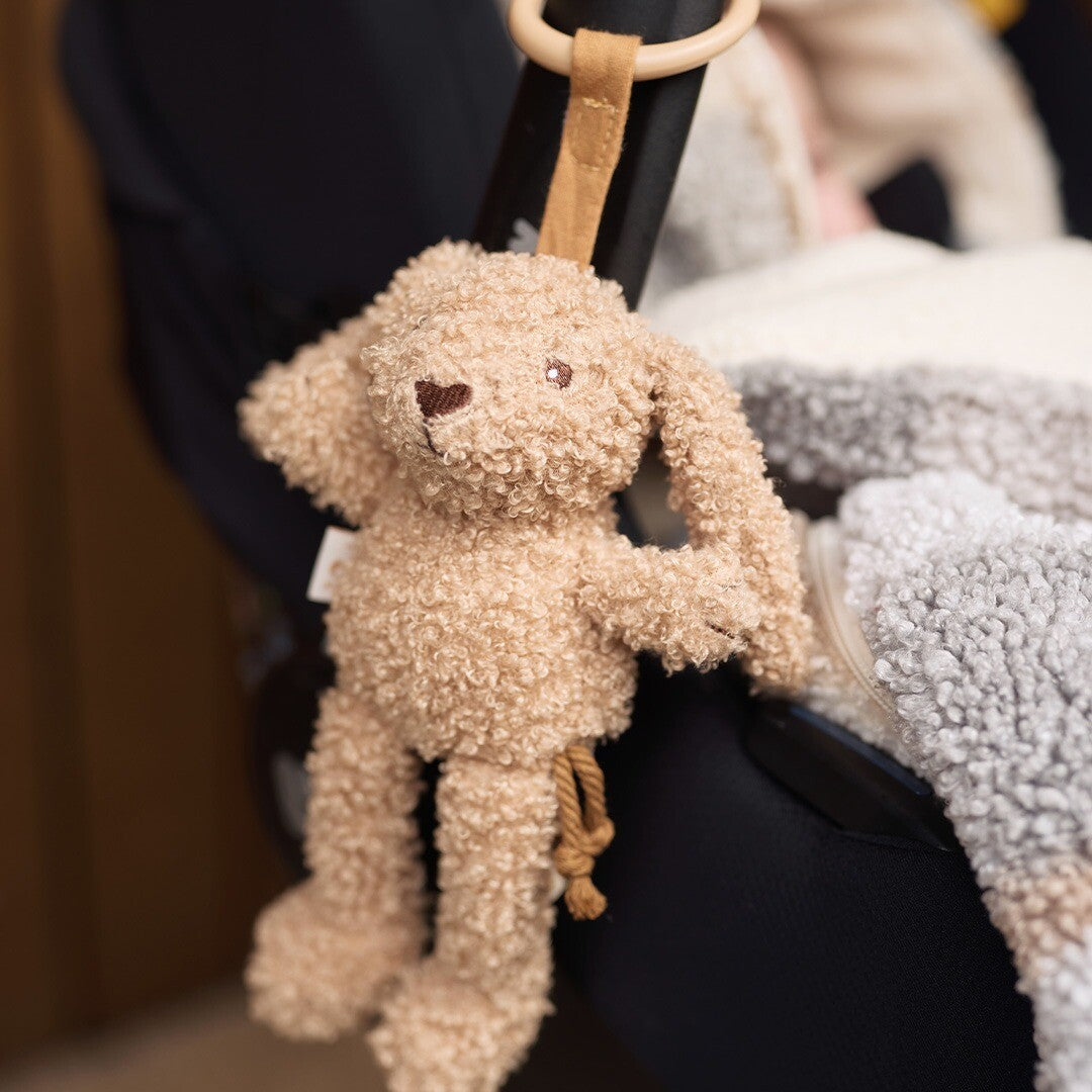 De Jollein wagenhanger in de vorm van een beige konijn hangt aan een zwarte kinderwagen.