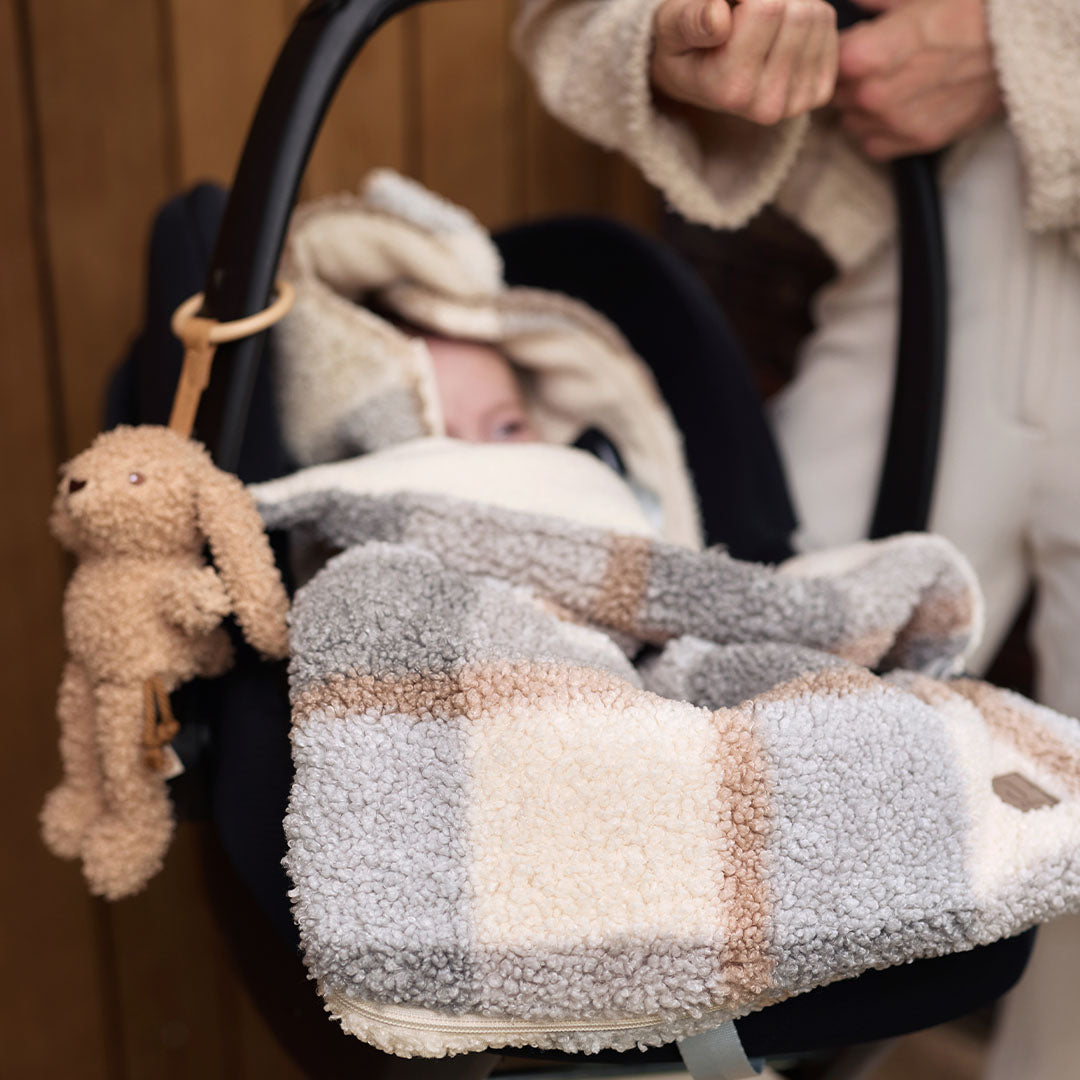 De Jollein wagenhanger in de vorm van een beige konijn hangt aan een autostoel met een baby en een plaid.