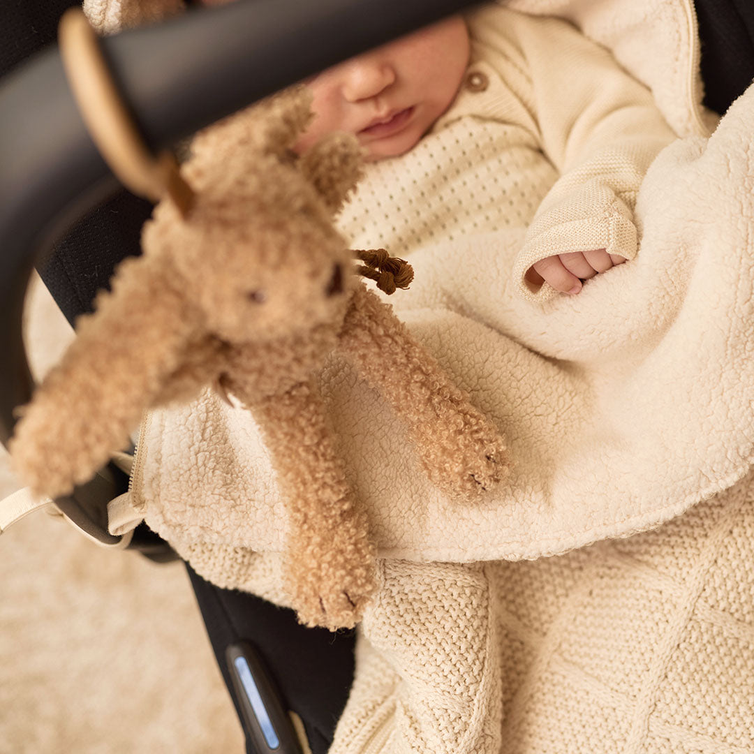 De Jollein wagenhanger in de vorm van een beige konijn hangt aan een autostoel met een baby in een crèmekleurige deken.