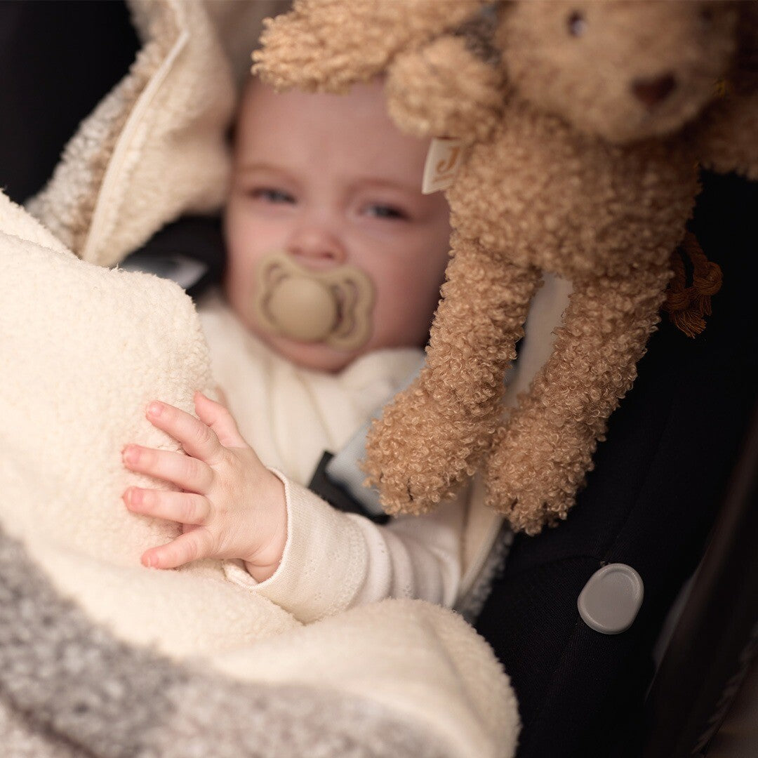 De Jollein wagenhanger in de vorm van een beige konijn hangt aan een autostoel met een baby met speen.