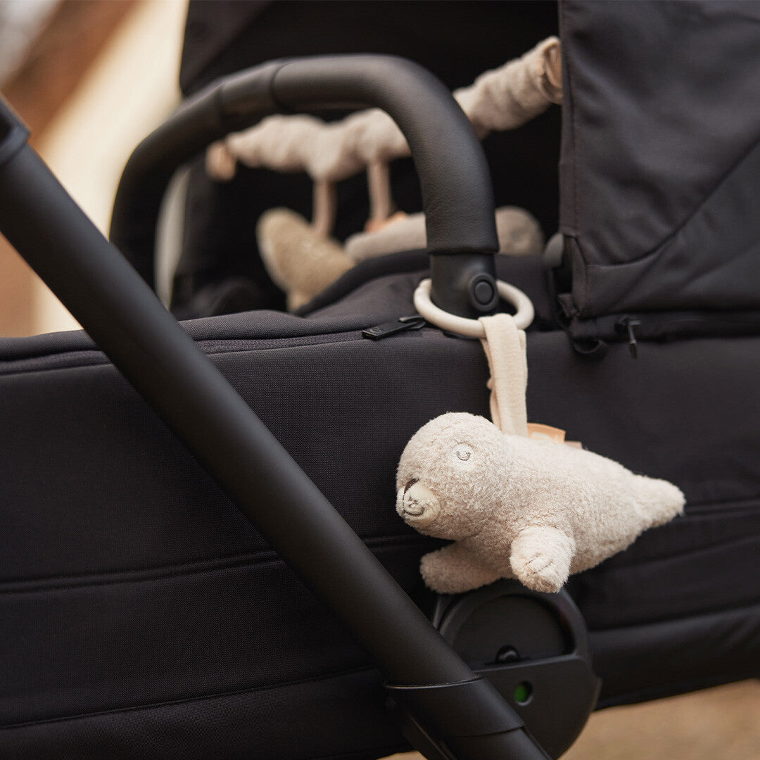 Jollein wagenhanger in de vorm van een pluche zeehond hangend aan de duwstang van een zwarte kinderwagen.