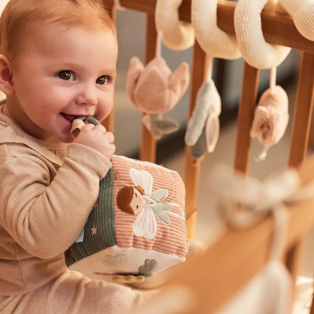 Een lachende baby speelt in een wieg met de Jollein activiteitenkubus met een fee.
