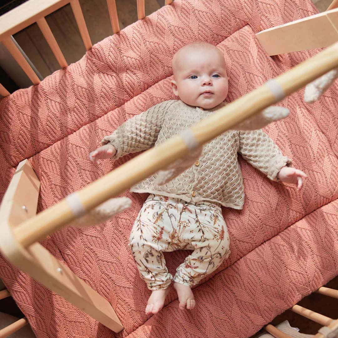Een baby ligt in een wieg onder de Jollein babygym met beige ster- en maanspeeltjes.