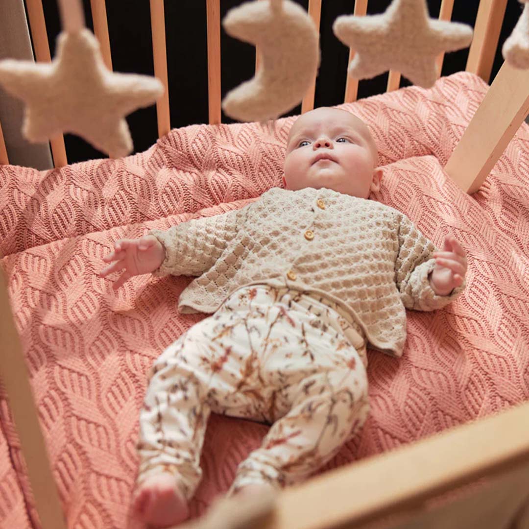 Een baby kijkt omhoog naar de beige ster- en maanspeeltjes van de Jollein babygym in een wieg.