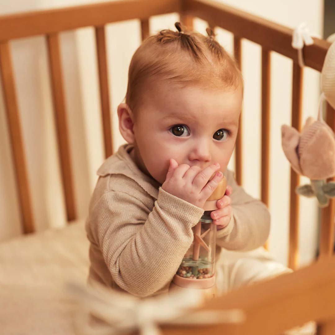 Een baby in een houten ledikantje speelt met de regenrammelaar.