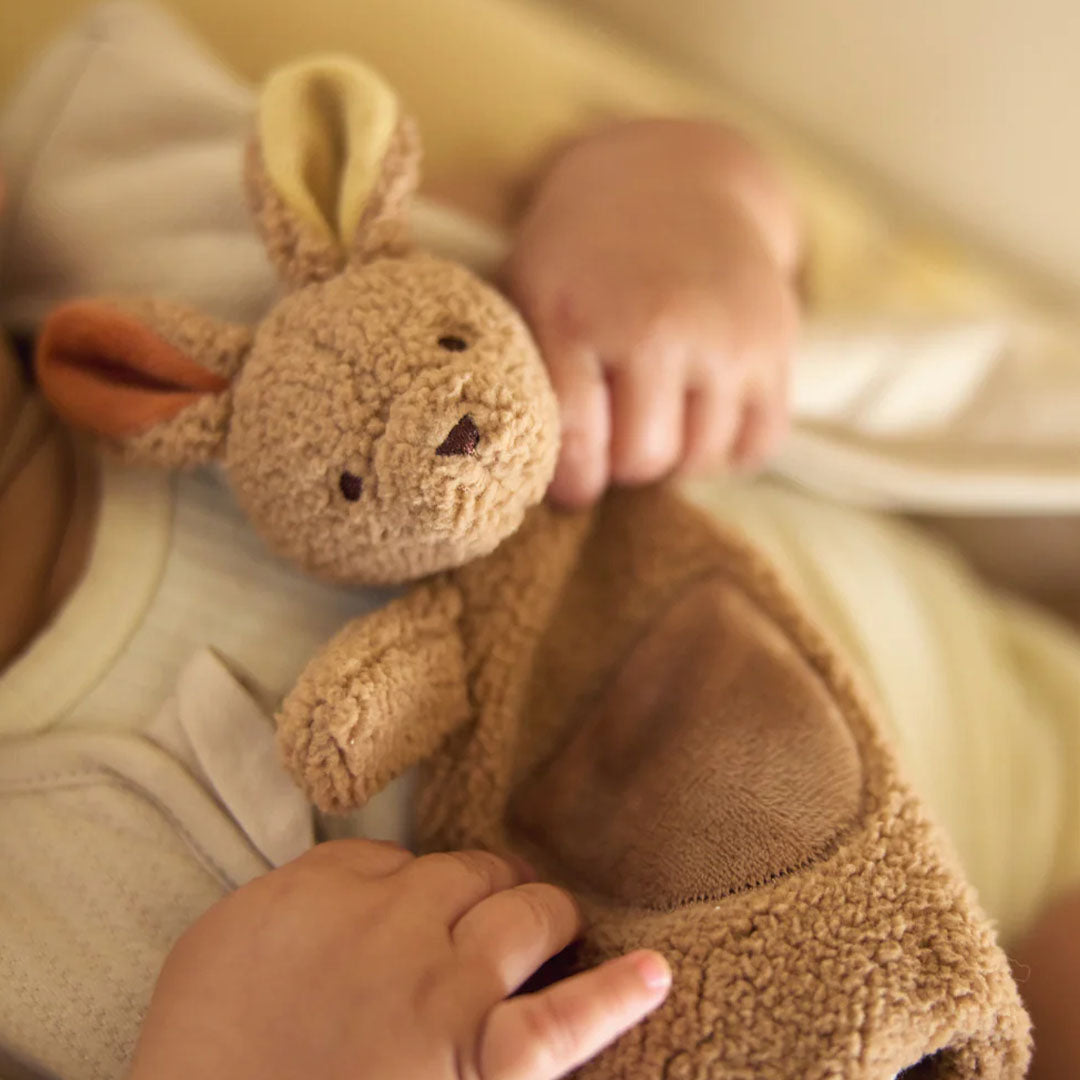 Een baby houdt de Jollein bruine kangoeroe speendoek vast.