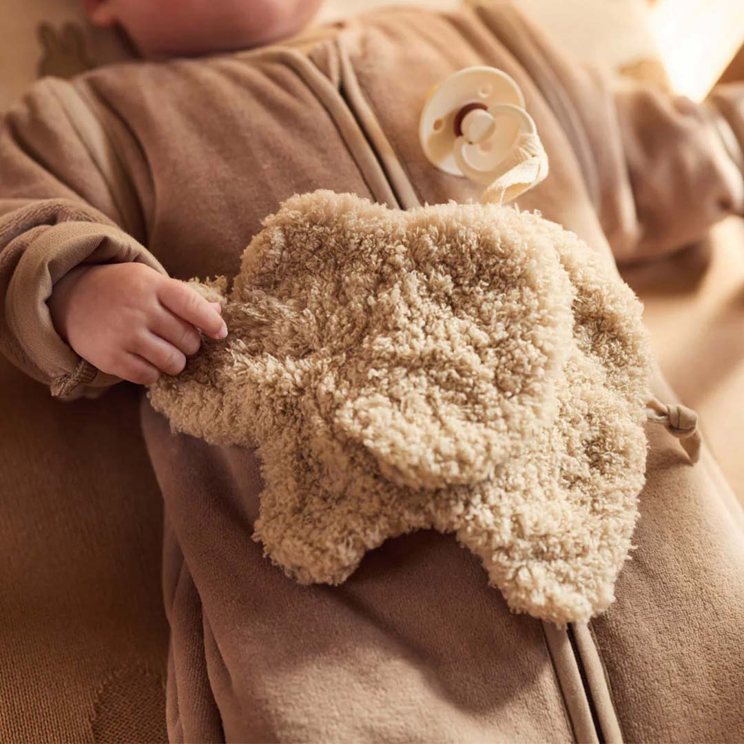 Een babyhandje houdt de Jollein olifant speendoek vast, de baby draagt een beige slaapzak.
