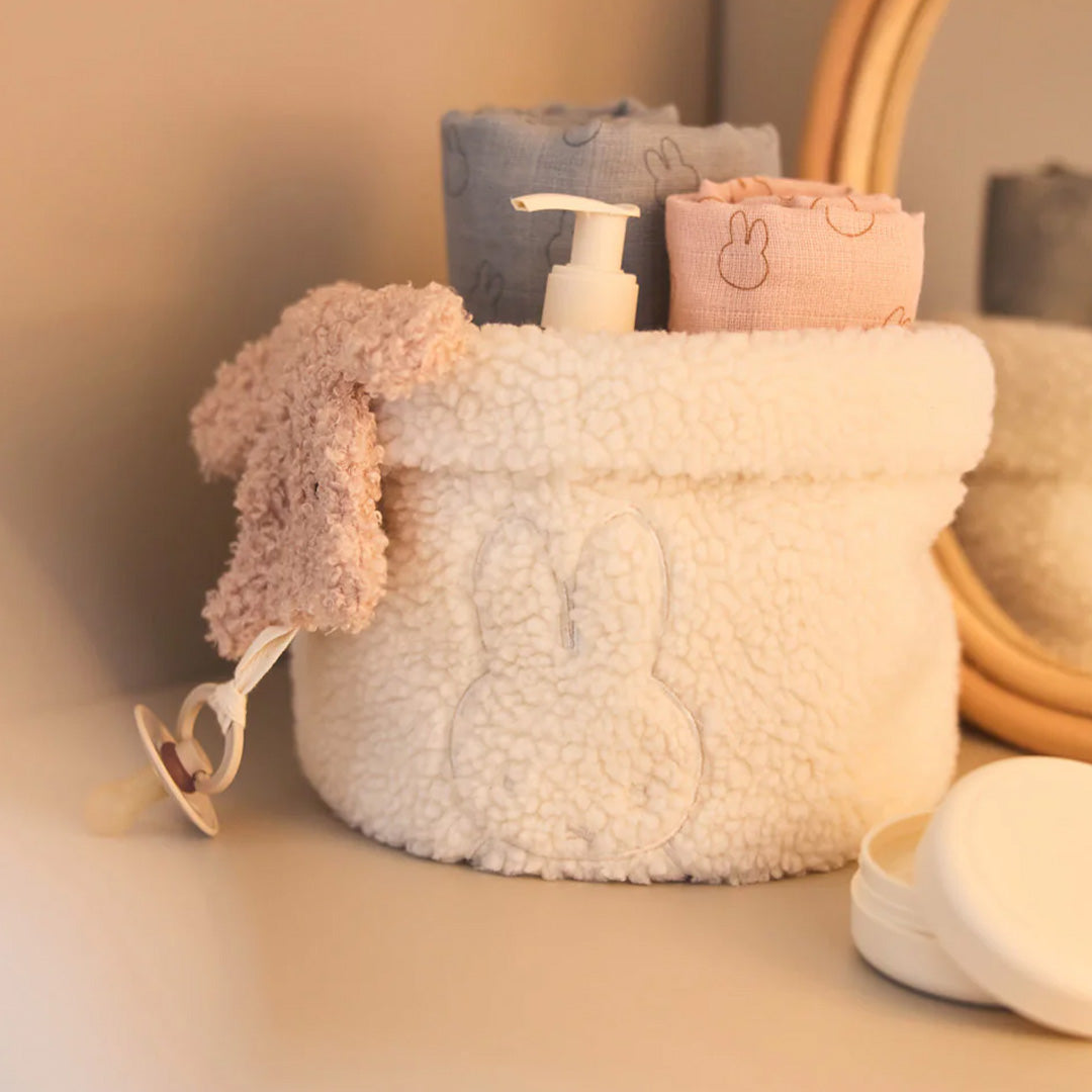 De Jollein speendoek in de vorm van een roze teddybeer hangt uit een witte opbergmand met een Nijntje-design.