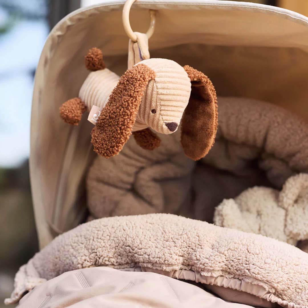 De Jollein wagenhanger in de vorm van een pluche hond hangt in een beige kinderwagen.